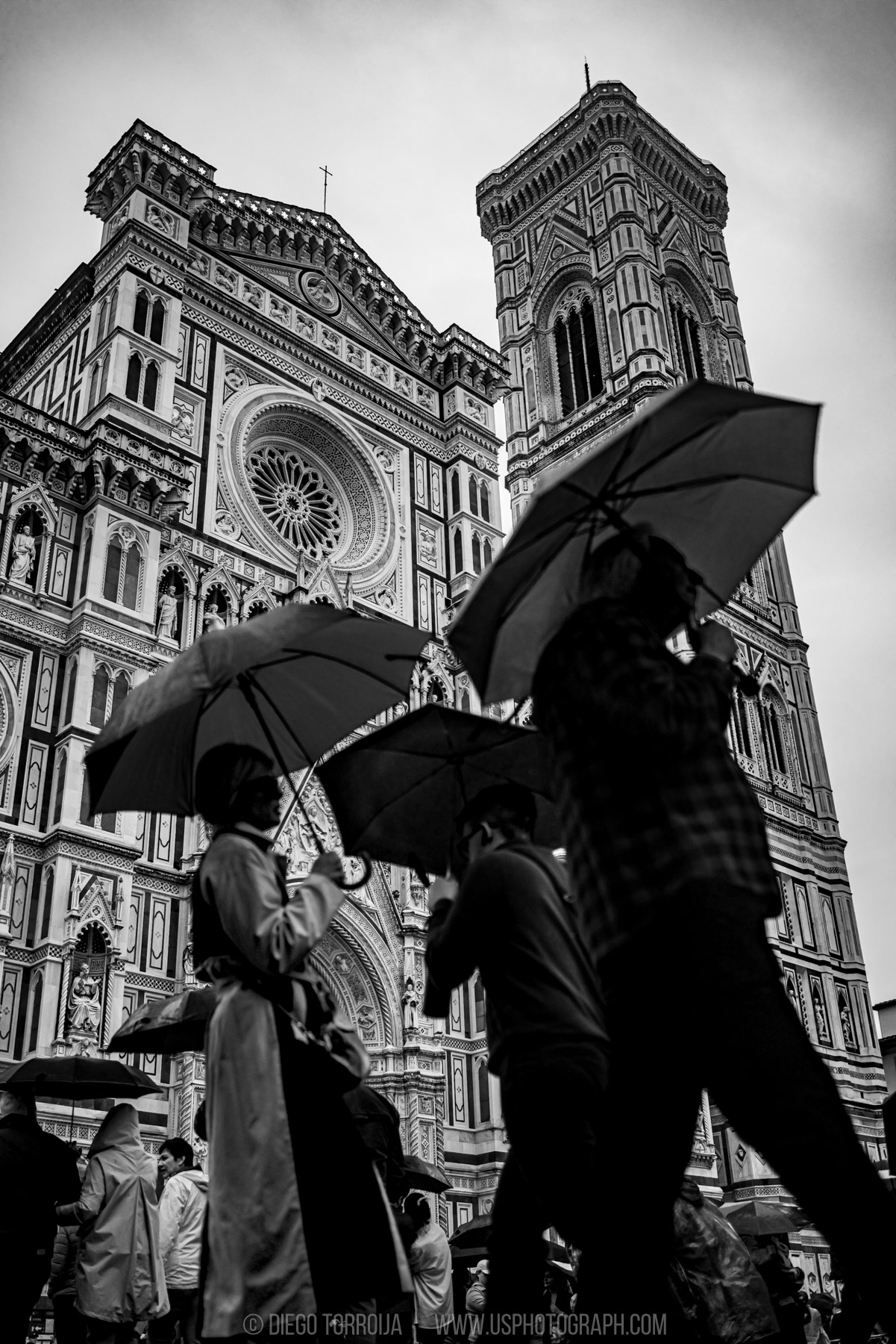 People with umbrellas below the Florence Cathedral facade and Giotto bell tower, black and white travel photo