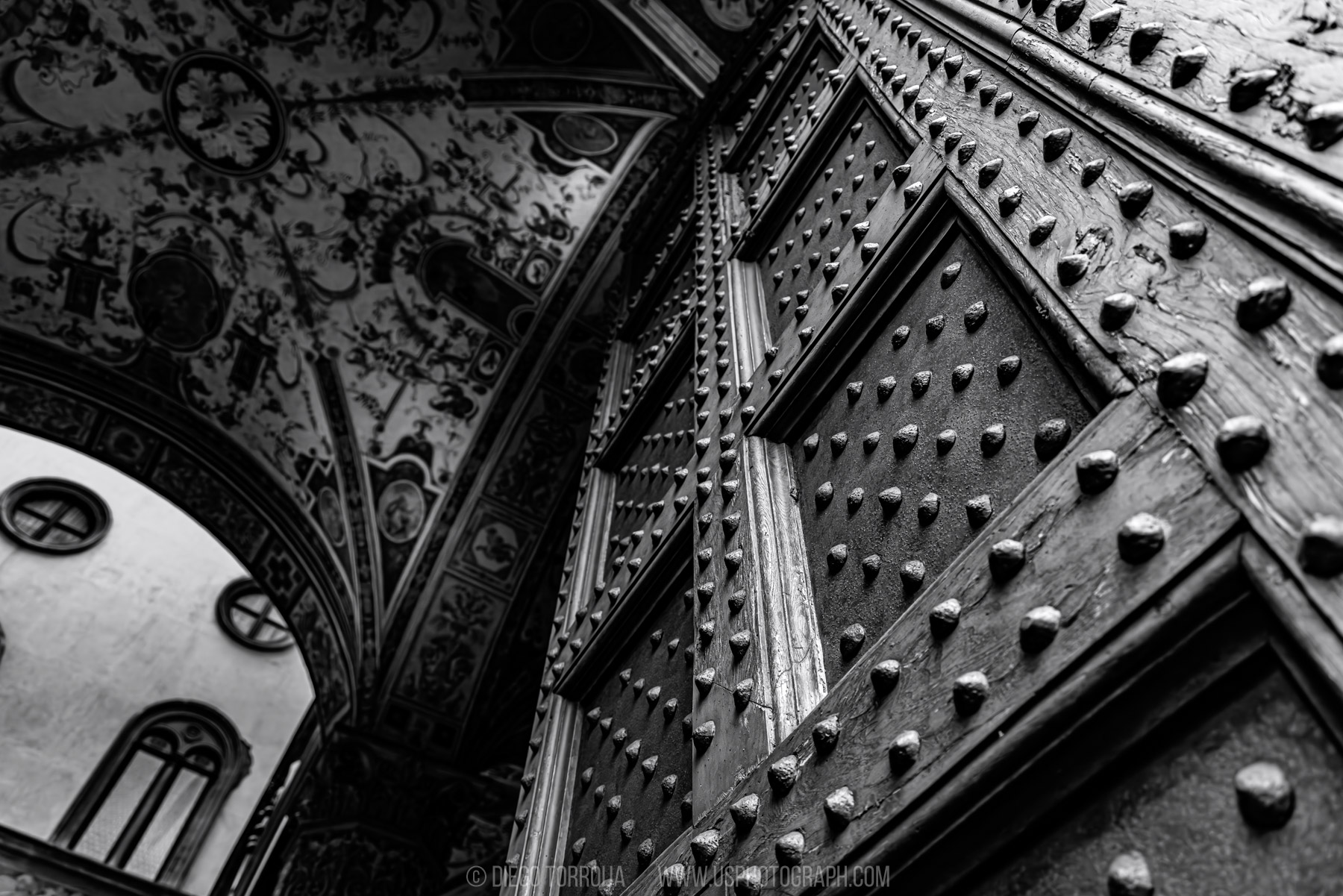 Massive studded wooden door beneath an ornate frescoed ceiling in Florence, black and white architectural detail