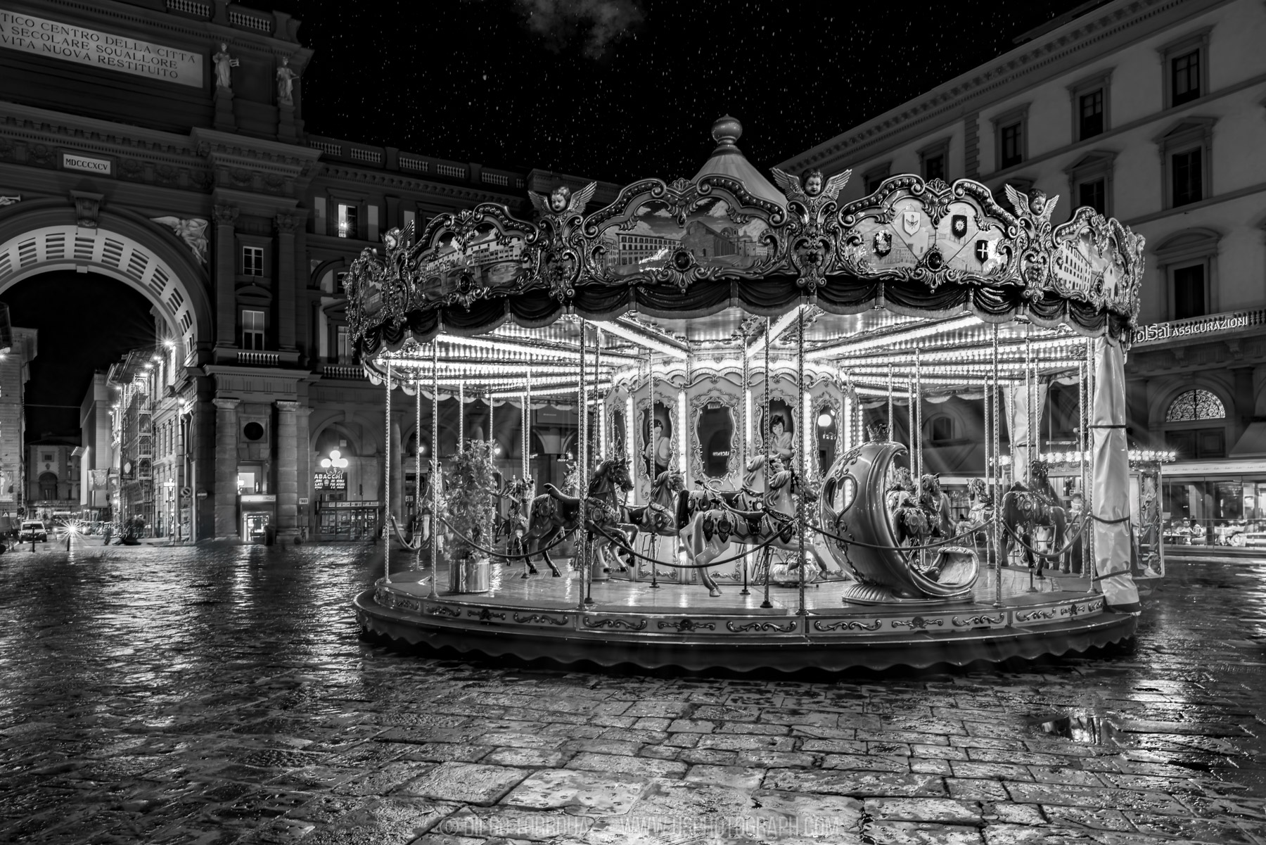 Illuminated carousel on wet cobblestones at night in Piazza della Repubblica, Florence, black and white photo