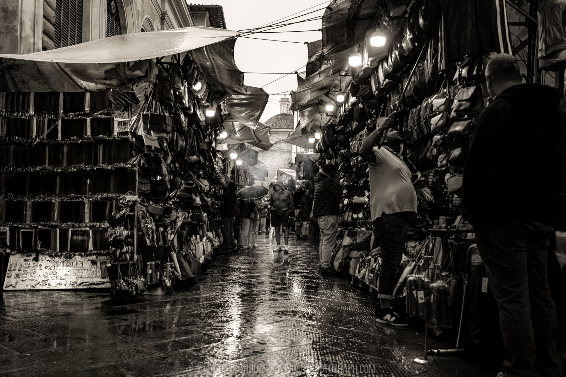 Rain-soaked street market lined with leather bags and glowing lights in Florence, sepia travel photography