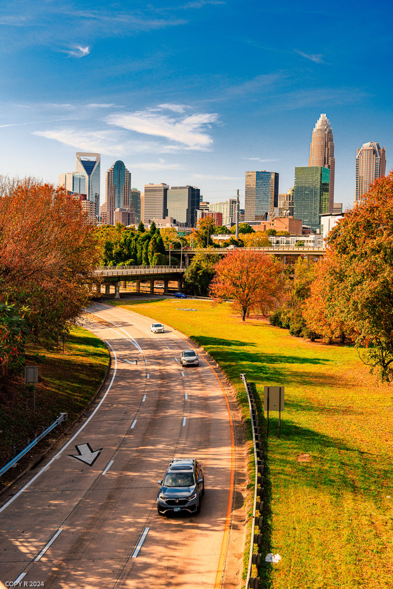 Road curving toward the uptown Charlotte skyline in autumn