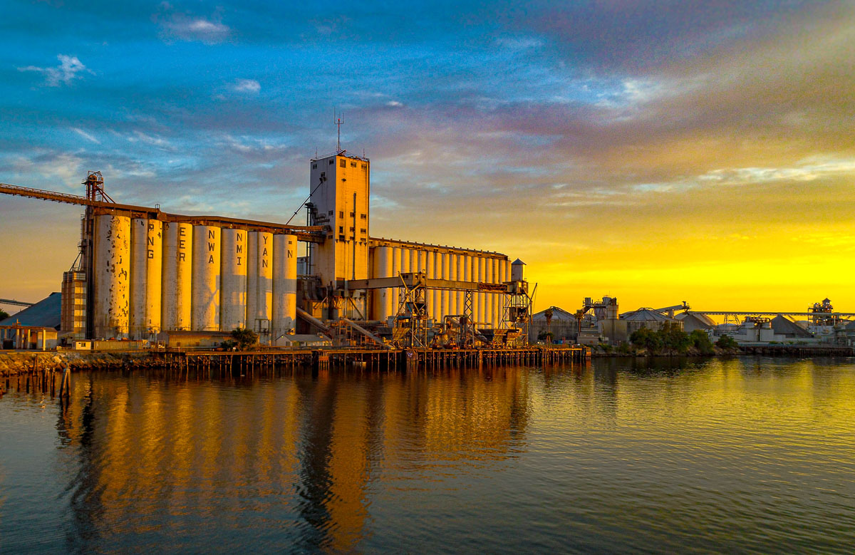 Industrial grain silos reflected in the water at golden sunset